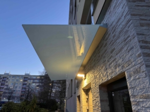 Skleněná stříška nad vchodem bytového domu v Třinci s mléčným sklem.