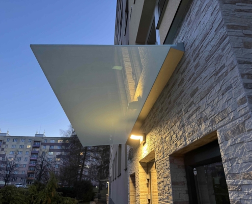 Skleněná stříška nad vchodem bytového domu v Třinci s mléčným sklem.